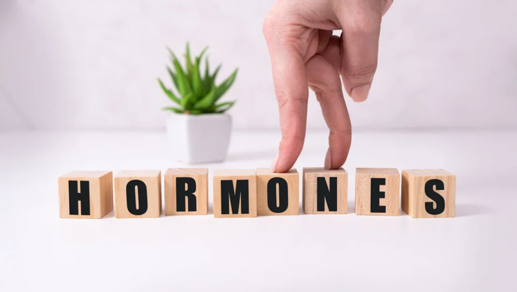Hand walking two fingers across wooden blocks spelling the word hormones, representing common signs of hormone imbalance.