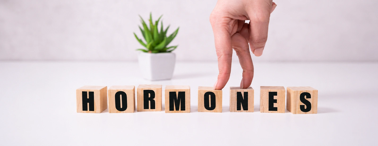 Fingers stepping across wooden letter blocks that spell hormones, illustrating gradual shifts in hormone balance.