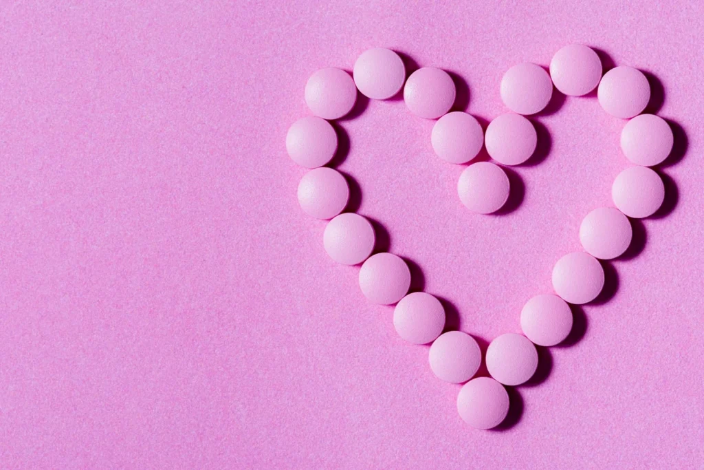 Pink round tablets arranged in a heart shape on a pink background, representing bioidentical hormone therapy options.