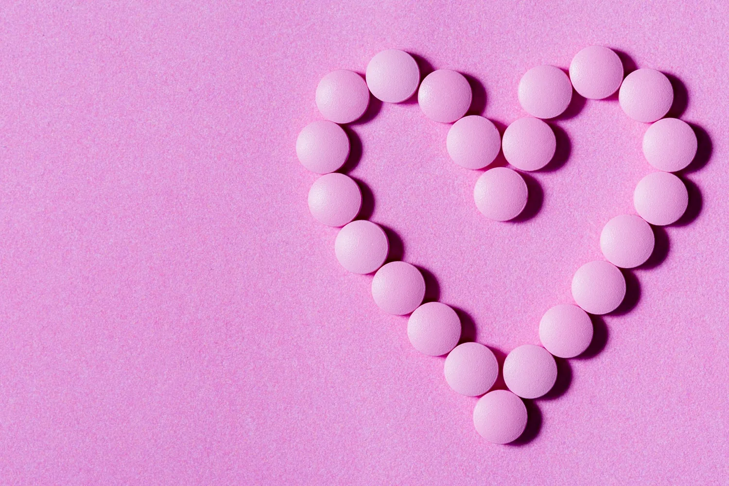 Pink round tablets arranged in a heart shape on a pink background, representing bioidentical hormone therapy options.